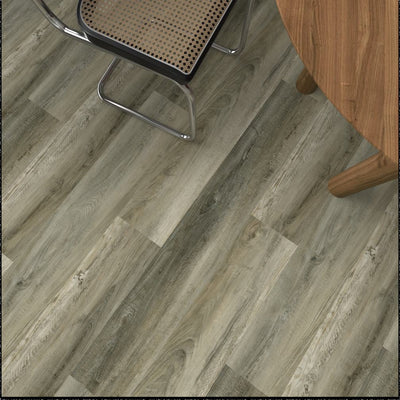 Gray-brown wood-look vinyl plank flooring shown from an overhead angle, with parts of a chair and a wooden table visible in the scene.